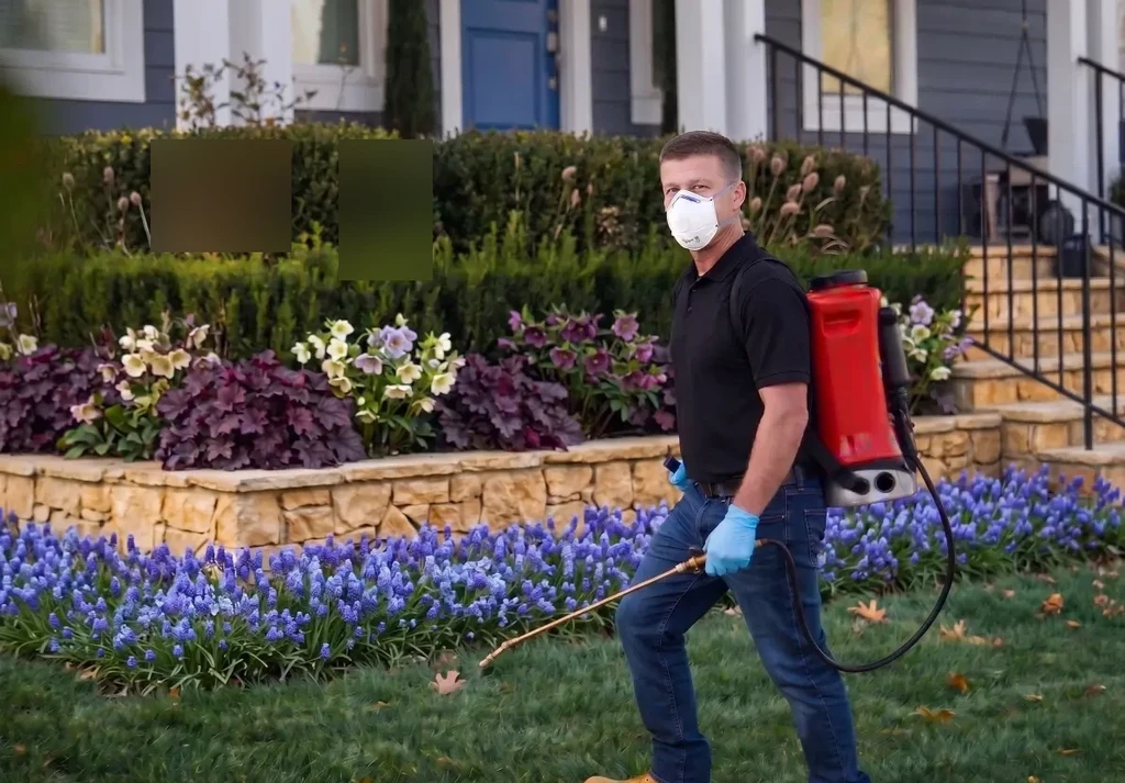 Pest control technician in protective mask treating a residential yard with a backpack sprayer in Bloomington, Indiana